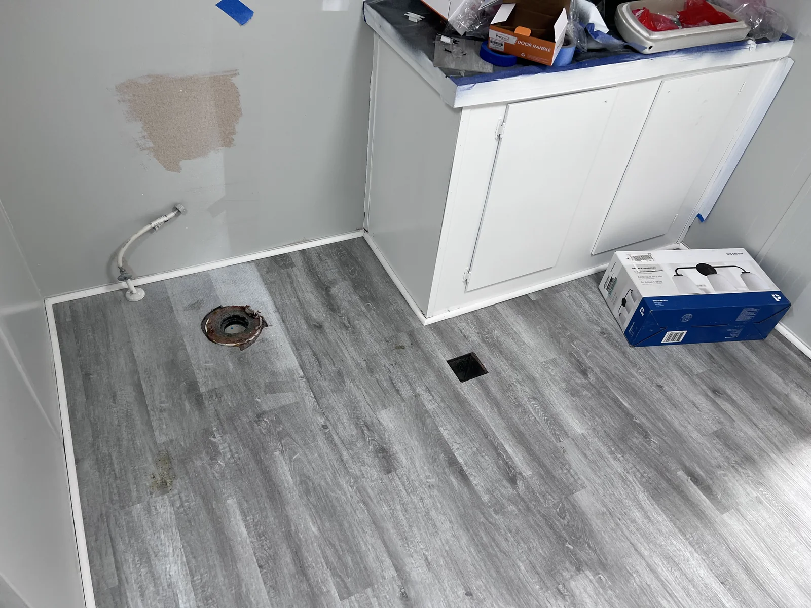 Bathroom in progress with white vanity, flooring and an open toilet flange