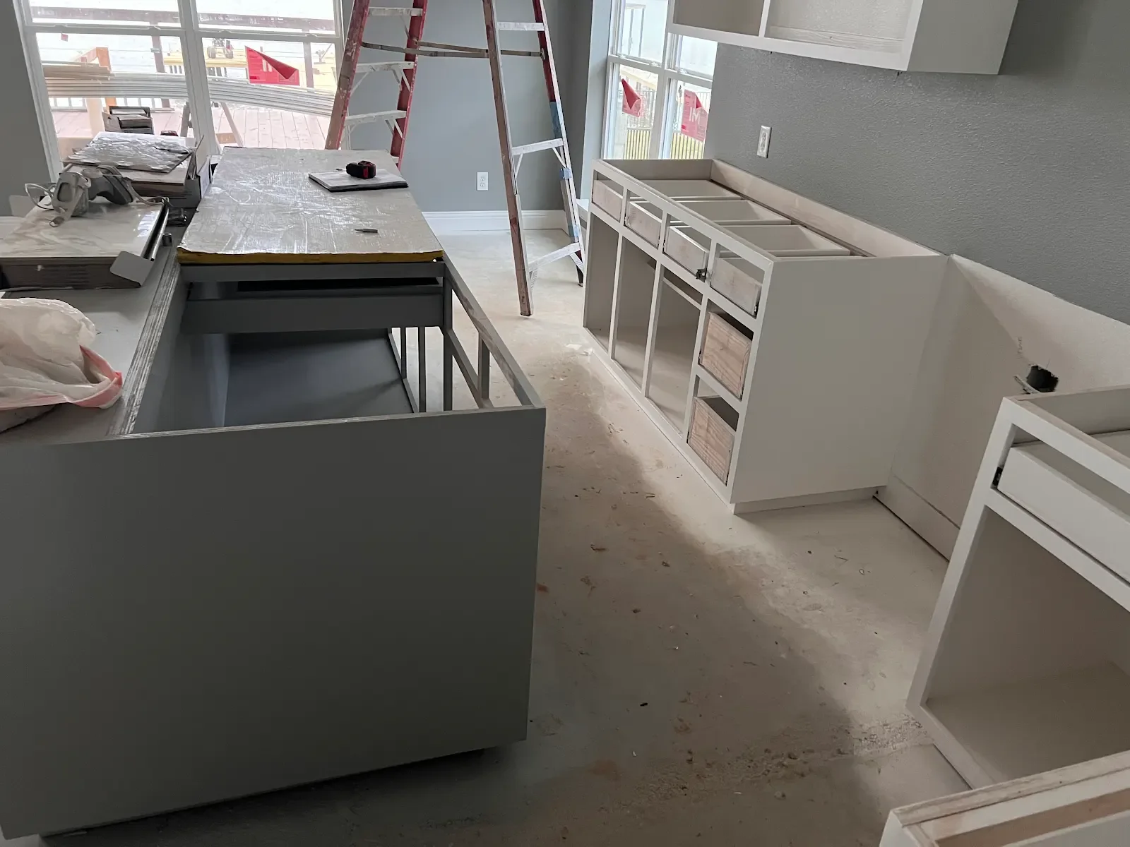 Kitchen cabinetry and island during installation with a ladder beside the windows