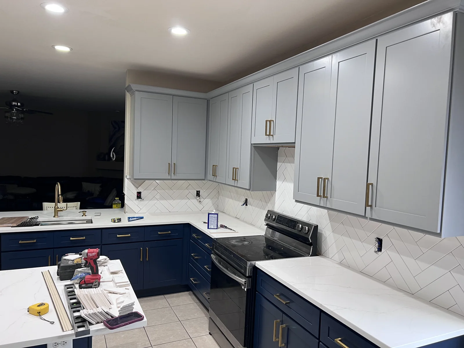 Kitchen with navy lower cabinets, pale upper cabinets, white backsplash and tools on the island