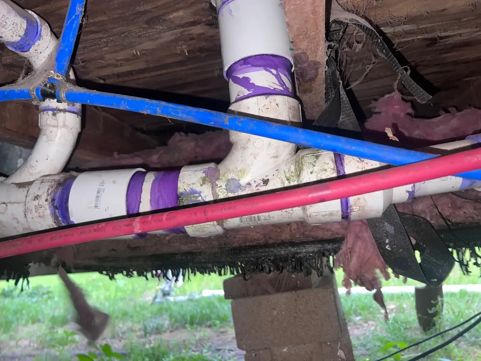 White drain fittings and red and blue water lines beneath a raised floor